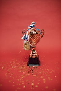 Golden trophy adorned with medals on a red backdrop surrounded by scattered confetti.