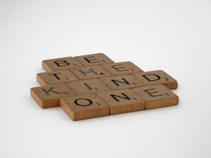 Wooden Scrabble tiles arranged to spell 'Be the Kind One', promoting kindness.